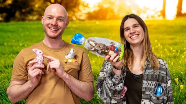 Ein junger Mann und eine junge Frau halten Schoko-Osterhasen in die Kamera und lachen