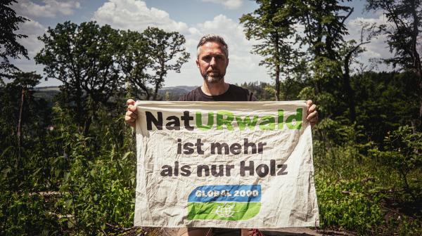 Dominik Linhard mit einem Banner im Wald: "NatURwald ist mehr als nur Holz"