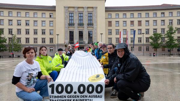 Vertreterinnen von Bürgerinitiativen, Vereinen und Naturzschutzorganisationen halten Banner mit 100.000 Unterschriften vor Landhaus in Innsbruck