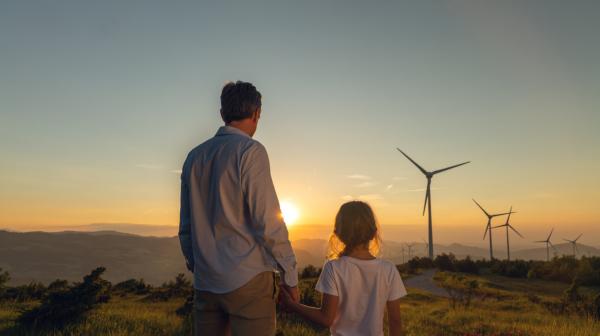 Mann und Kind schauen in eine Landschaft mit Sonnenunter- oder aufgang, in der Windräder stehen