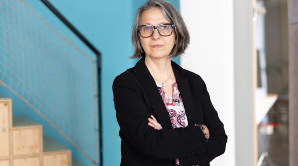 GLOBAL 2000 Geschäftsführerin Alexandra Strickner steht mit verschränkten Armen vor einer blauweissen Wand