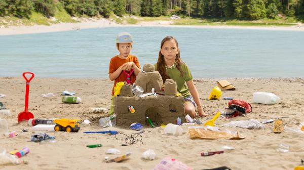 2 Kinder bauen eine Sandburg mit Müll vor österreichischer Landschaft
