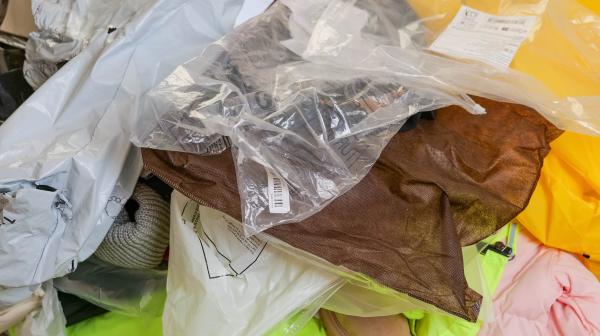 Viele Kleidungsstücke übereinander, darüber und darunter die Plastikverpackung.