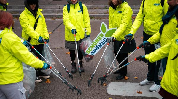 GLOBAL 2000-Freiwillige in grünen Jacken stehen im Kreis und werden Müllsammeln