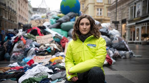 Anna Leitner, Ressourcensprecherin von GLOBAL 2000, hockt vor Müllberg mit Kleidung in der Wiener Innenstadt