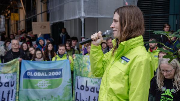 Hannah Keller spricht vor Demonstrant:innen, die Banner halten mit der Aufschrift Lobau bleibt und GLOBAL 2000