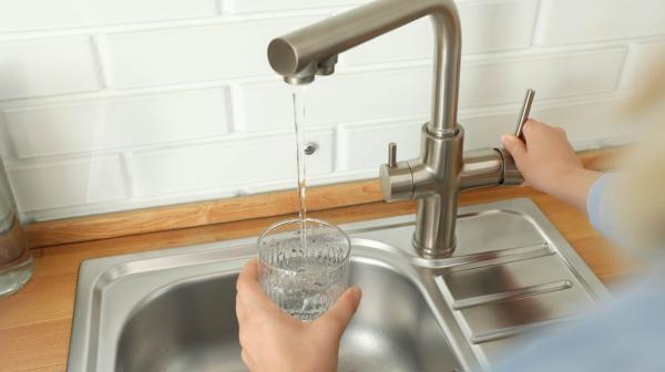 Wasserhahn über Spüle, aus dem Wasser in ein Glas fließt, Hand hält das Glas und betätigt den Hebel