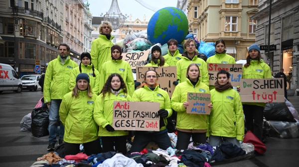 Aktivist:innen von GLOBAL 2000 protestieren mit Kleidungsberg und Erdball für Anti-Fast-Fashion-Gesetz