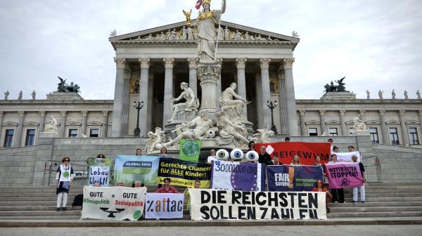 Viele Menschen mit Bannern stehen vor dem österreichischen Parlament. Zentral ist ein Banner auf dem steht "Die Reichsten sollen zahlen"