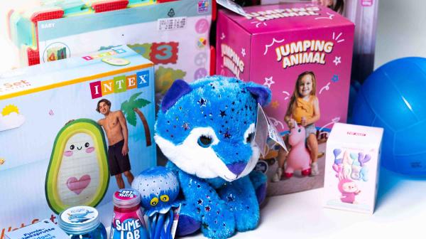 Verschiedene bunte Spielzeuge, darunter ein blaues Plüschkätzchen mit Sternen, ein aufblasbares Planschbecken mit Pinguinmotiv, ein rosa hüpfendes Tier auf einer Verpackung mit der Aufschrift 'JUMPING ANIMAL' und mehrere kleine Spielzeugbehälter und -flaschen