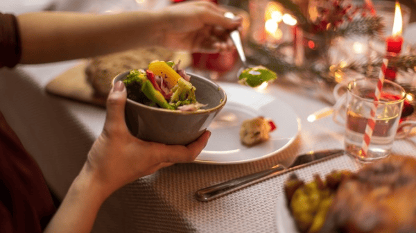 Hand hält Schüssel mit vegetarischem Essen am festlich gedeckten Tisch
