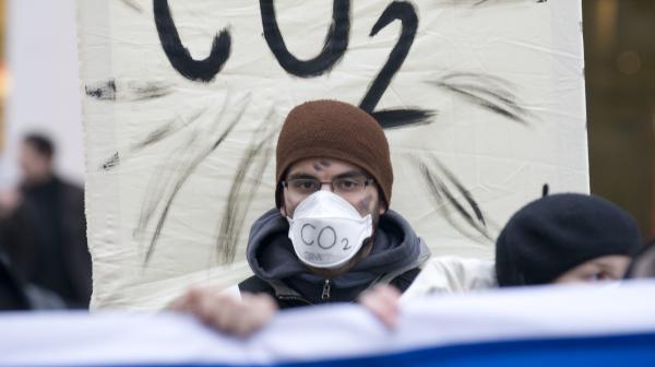 Mann mit Maske vor Plakat auf dem CO2 steht.