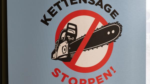 Ein graues Schild auf dem steht: Kettensäge stoppten! Menschen und Umwelt schützen