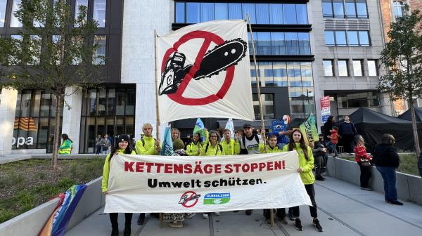 Gruppe von Menschen demonstriert gegen die Kettensäge mit großen Plakaten, die einen besseren Schutz der Umwelt fordern. 